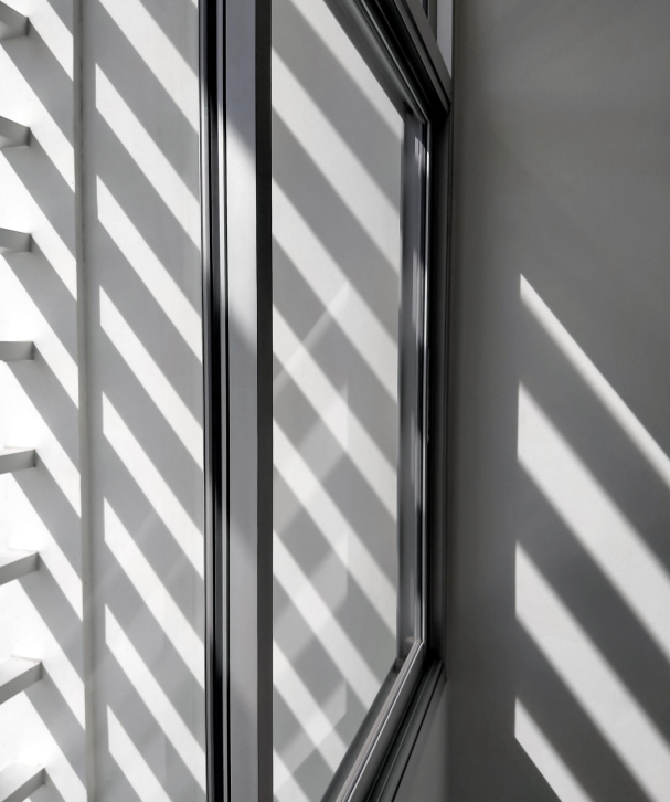 Selective focus at glass window sill, side view and diagonal pattern of sunlight and shadow shining through from outside of building in black and white style